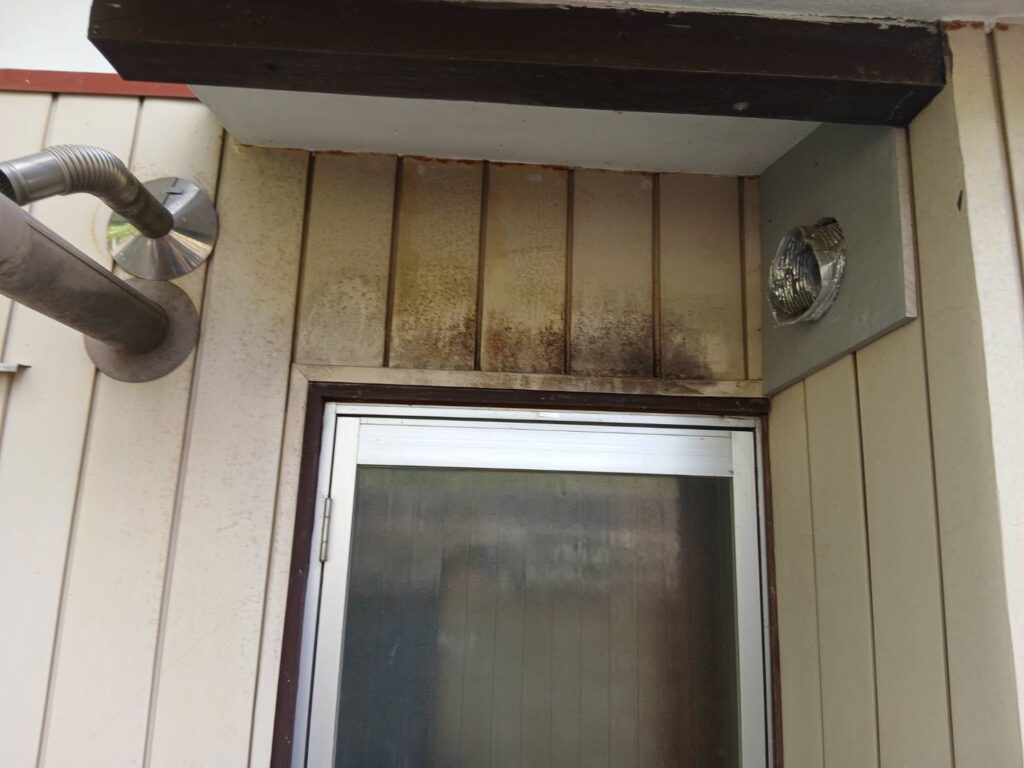 住宅外壁の換気口まわりに発生した黒カビと汚れの様子。湿気がこもりやすい場所で外壁が変色している状態を示す。