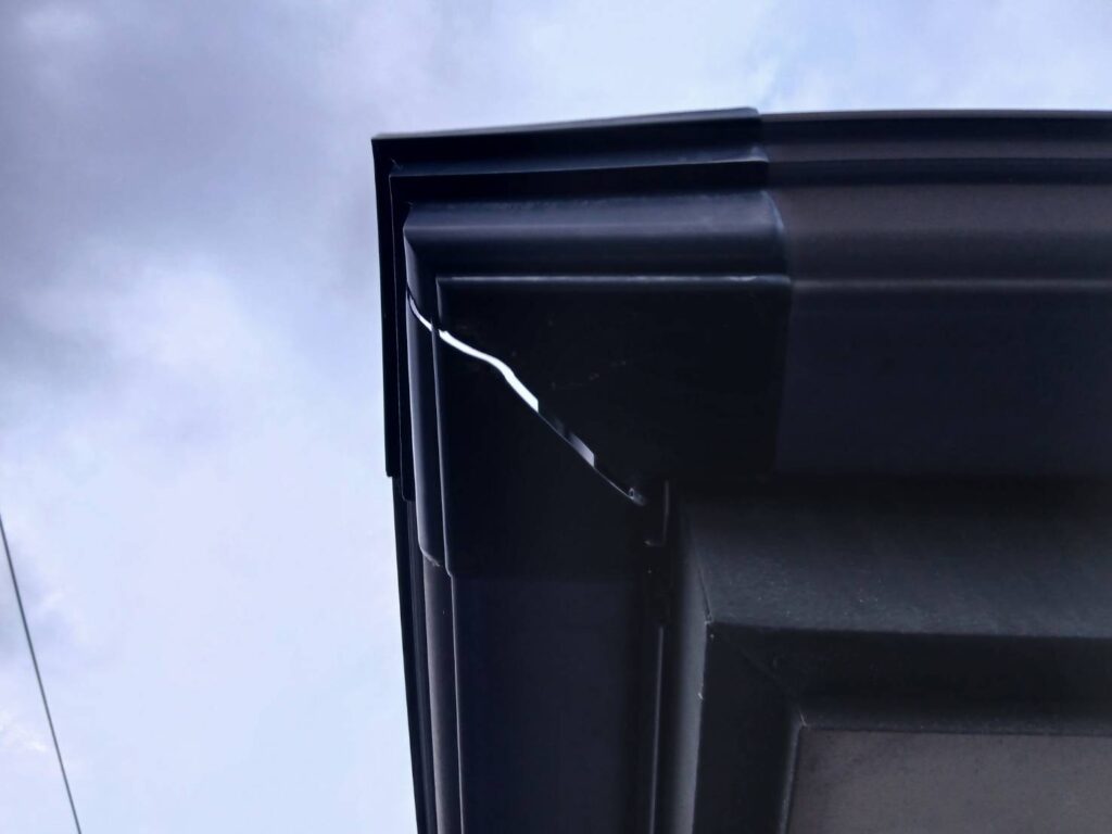 雨樋の一部が割れて穴があいている状態。排水時に雨水が漏れ出している。