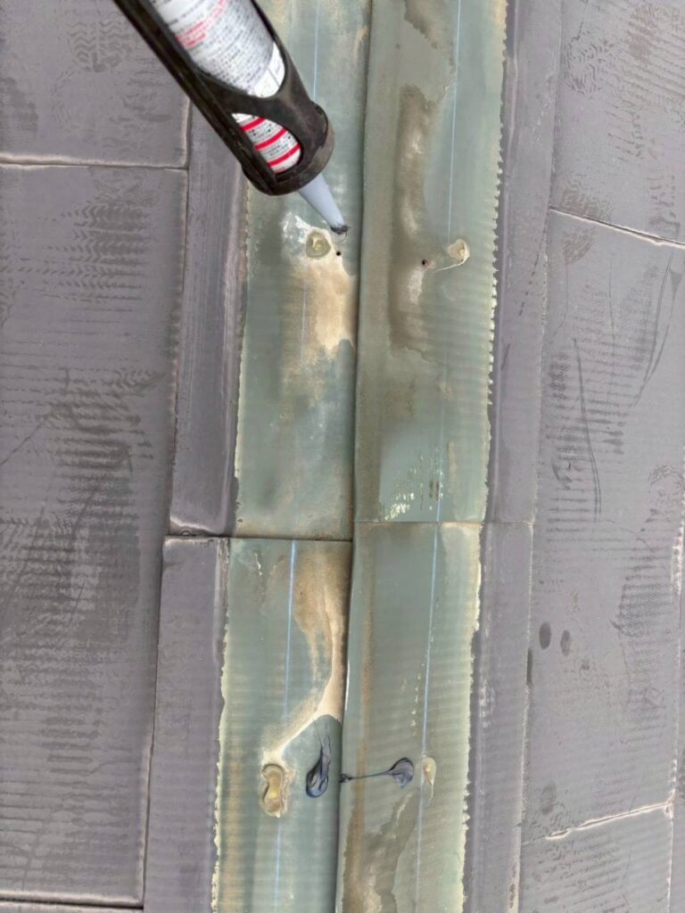 棟板金の釘穴をコーキングで埋めて防水処理している様子