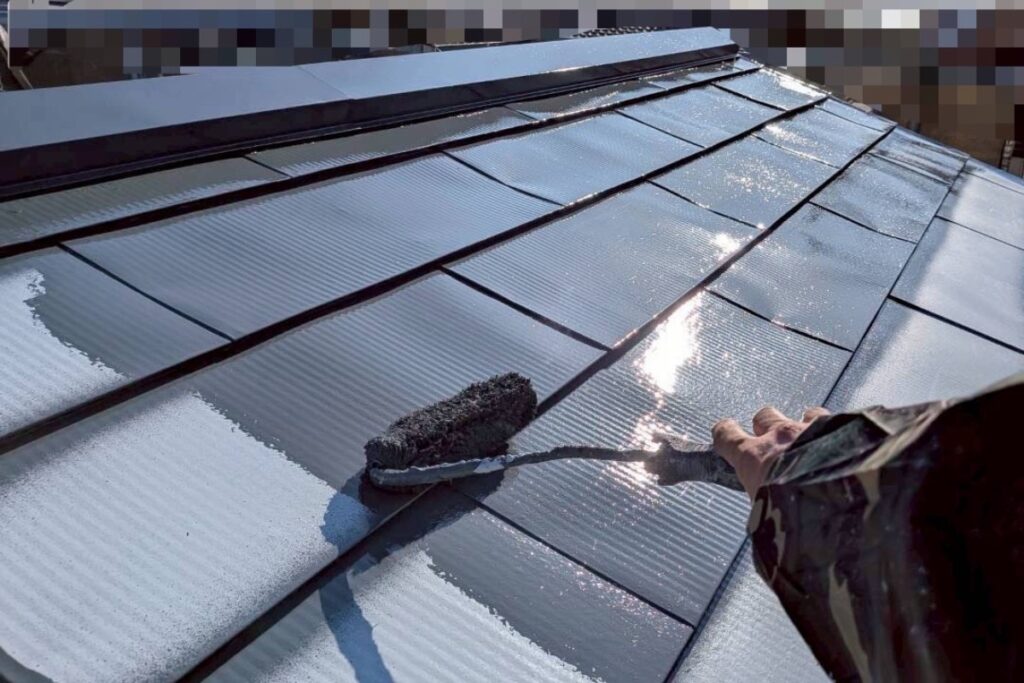 屋根の中塗り塗装をローラーで丁寧に仕上げている職人の手元