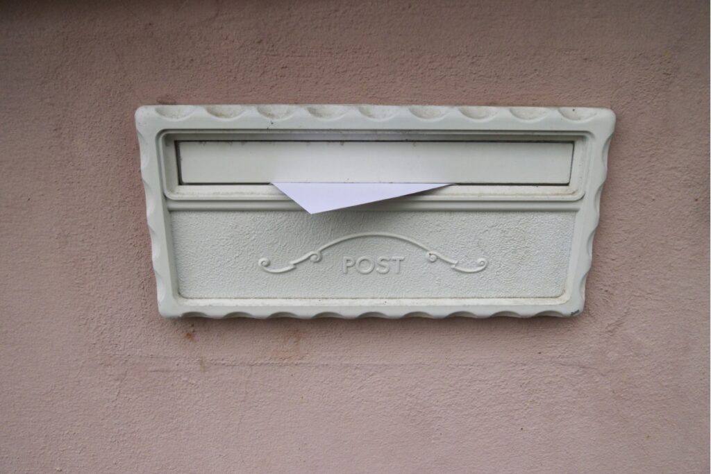 壁に直接取り付けられた壁付けタイプの郵便ポスト。投入口に郵便物が差し込まれている様子。