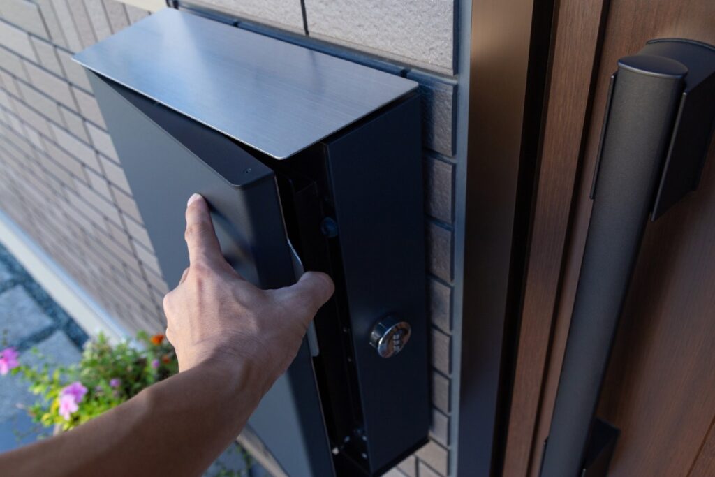 玄関横の外壁に後付け設置されたブラックカラーの郵便ポストを開けている様子。
