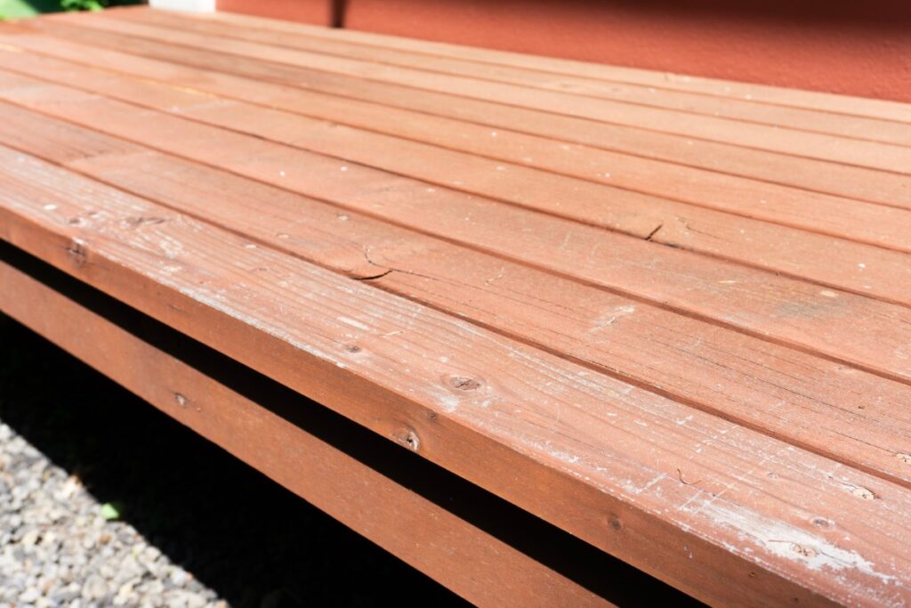 表面の色あせや細かなひび割れが見られる劣化したウッドデッキの木材写真