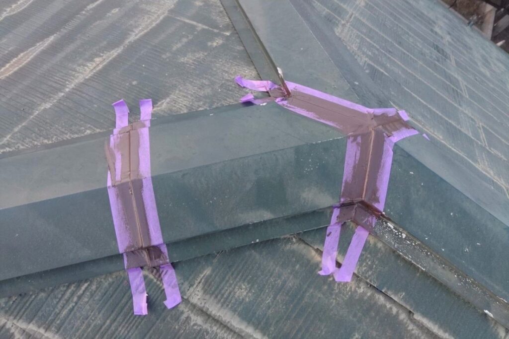 棟板金の継ぎ目にコーキング処理を行っている屋根補修作業の様子