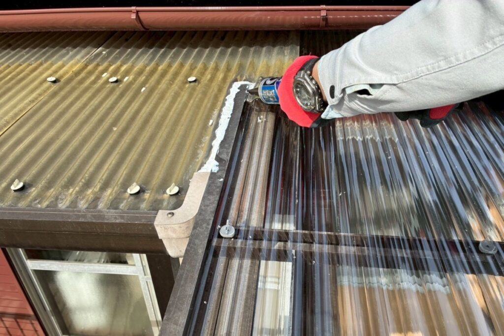 波板屋根の接合部にコーキング処理を行っている様子